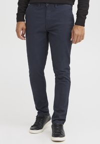 Tamnoplavi chinos s uskim krojem, s kop�čanjem na dugme i džepovima, u kombinaciji s crnim tenisicama i crnom sweatshirtom.