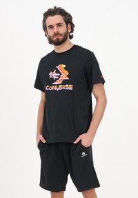 Tricou negru din bumbac cu un model colorat de nori și textul "CONVERSE". Purtați cu șorturi negre ce prezintă un logo pe partea stângă.
