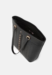 Sac fourre-tout noir avec motif en relief, détail chaîne dorée, double poignée et compartiment principal ouvert avec poche à fermeture éclair à l'intérieur.