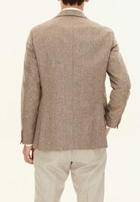 Brauner Fischgrät-Blazer mit taillierter Passform, Reverskragen und einfachem Rückenschlitz. Kombiniert mit hellbeigen Hosen.