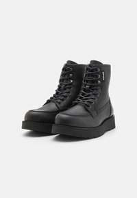 Schwarze Leder-Stiefeletten mit Schnürdesign und gepolstertem Kragen. Sie haben eine robusten Gummisohle und dezente Nähtdetails.