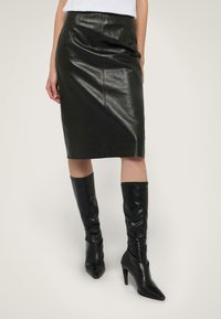 Schwarzer Leder-Bleistiftrock mit glatter Textur, hohem Bund und knielanger Schnitt, kombiniert mit enganliegenden schwarzen Stiefeln bis zum Knie.