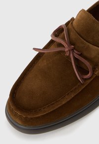 Brown suede loafers with a rounded toe, featuring a matching brown leather lace. The sole is dark and slightly elevated.
