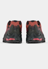 Μαύρα και κόκκινα παπούτσια trail running με υφή στο επάνω μέρος, ενισχυμένη φτέρνα και ανθεκτική σόλα για καλύτερη πρόσφυση. Σημασία ορατή στις πλευρές.