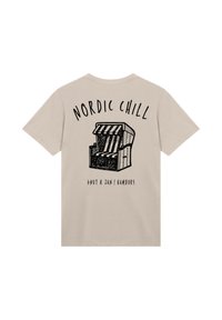 Beige T-Shirt mit schwarzer Illustration eines gestreiften Strandstuhls und dem Text "NORDIC CHILL" darüber sowie "KNUT & JAN | HAMBURG" darunter.
