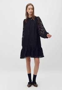 Rochie neagră cu un model floral, cu mâneci lungi din material transparent, nasturi în față și tiv ondulat. Stilizată cu șosete închise la culoare și balerini maro.
