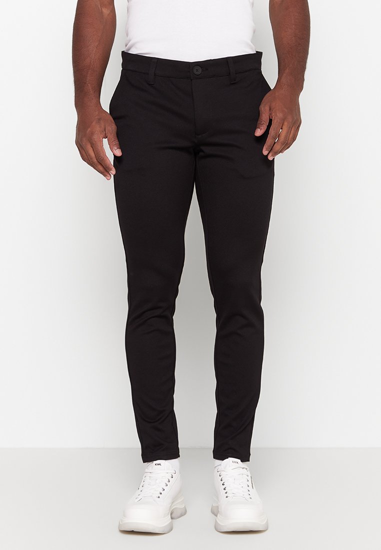 Black slim-fit pants made of woven material, featuring a button closure, belt loops, and front pockets. Paired with white sneakers.
