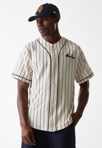 Cream striped baseball jersey with black vertical lines, button front, rounded collar, and embroidered "New Era" logo. Paired with a navy cap.