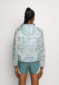 Chaqueta ligera con capucha en verde menta con un patrón de camuflaje, puños elásticos y un ribete negro a lo largo del dobladillo.