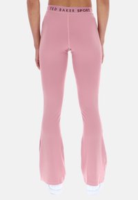 Różowe legginsy dzwonowe wykonane z elastycznej tkaniny, z wysokim pasem z logo "TED BAKER SPORT" oraz rozporkami po bokach u dołu.
