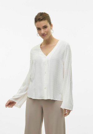 Witte blouse met een V-hals, lange mouwen en knoopsluiting. Heeft een textuur met stippenpatroon en een ontspannen pasvorm.