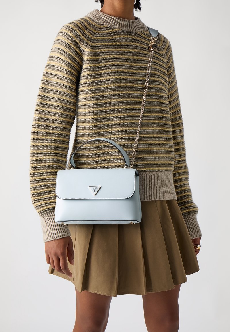 Persona che indossa un maglione a righe gialle e grigie e una gonna a pieghe marrone, mentre tiene una borsa azzurro chiaro con tracolla a catena.