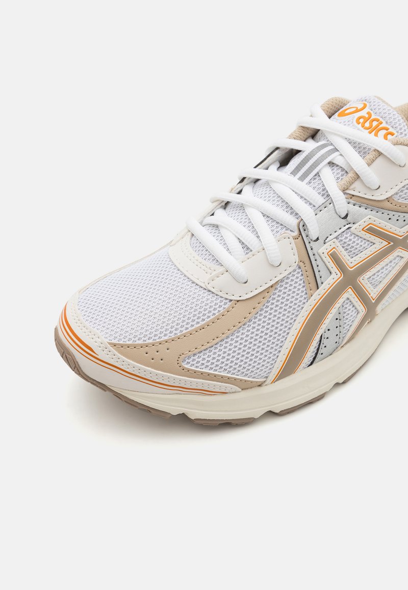 Weiße und beige Sportschuhe mit Obermaterial aus Mesh, gepolstertem Kragen, orangefarbenen Akzenten und Gummisohle mit Rillen für besseren Halt.