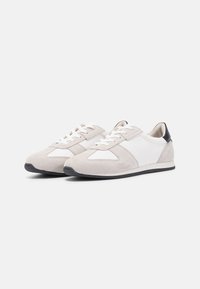 Semsket og lær sneakers i lys grå og hvit, med sort hælakkent, flate lisser og gummisåle med trekantede detaljer.