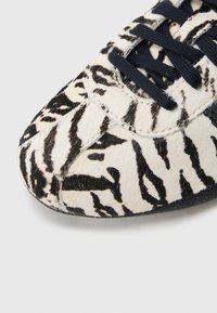 Υφασμάτινα πάνινα παπούτσια με υφή, με σχέδιο λευκού και μαύρου ζώου, με σκουρόχρωμους κορδόνια και μαύρη σόλα χαμηλού προφίλ.