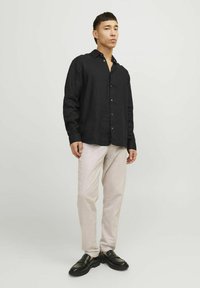 Camicia button-up nera in lino, vestibilità rilassata, maniche lunghe. Abbinata a pantaloni beige chiaro e mocassini neri. Design semplice, senza motivi.