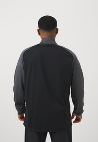 Zwarte en donkergrijze langemouwen shirt met een kraag; soepele textuur; aangesloten ontwerp met contrasterende schouderpanelen.