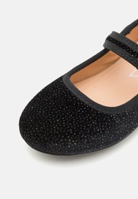 Zapato Mary Jane negro con parte superior texturizada con detalles brillantes, punta redonda y una correa negra contrastante. Forro interior liso.