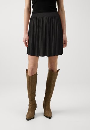 Black pleated skirt with a solid waistband, featuring a knee-length design. Worn with knee-high brown leather boots with pointed toes.