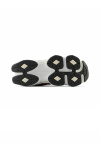 La suela de la zapatilla presenta una base de goma negra con troqueles hexagonales, acentos en blanco y beige, y una marca central en el talón.