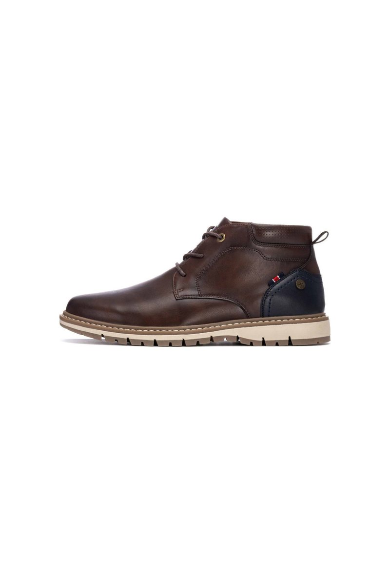 Botín chukka de cuero marrón con suela de goma beige y acento en el talón de color azul oscuro. Presenta cordones redondos y un lazo en la parte trasera para facilitar el calzado.