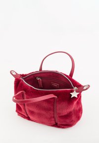 Bolso rojo y peludo con cierre de cremallera, dos asas cortas y un charm de estrella plateada. El interior cuenta con un bolsillo con cremallera y una etiqueta de marca.