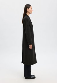 Randig lång kappa i mörkgrå ullblandning, med enkelknäppning, slagkrage och sidofickor, bärs över svarta jeans.