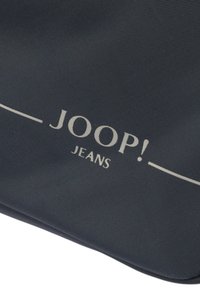 Mörkblå texturerad tygväska med en framträdande ljus färgad "JOOP! JEANS"-logotyp och minimalistisk design med rena linjer.