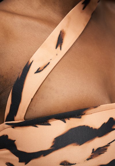 Κοντινό πλάνο στήθους ατόμου που φοράει κορυφή χιαστί σε ροδακινί και μαύρο με βαθιά λαιμόκοψη.