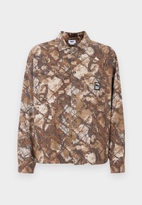 Barna és bézs álcázó mintázatú ing, mellzsebre és bal oldalon hímzett logó címkével.