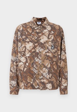 Kamo rašto marškiniai su mygtukais rudos ir smėlio spalvų, turintys krūtinės kišenę ir išsiuvinėtą logotipo etiketę kairėje pusėje.