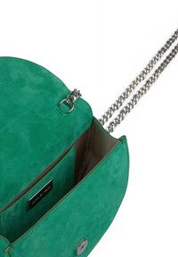 Bolso de ante verde con una correa de cadena metálica. Presenta una solapa redondeada y un interior suave con un compartimento para tarjetas. Acentos en metal plateado.