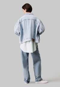 Lichtblauwe denimjas met een oversized pasvorm, verlaagde schouders en een verkorte onderkant. Gelaagd over een wit shirt en gecombineerd met lichtblauwe jeans.
