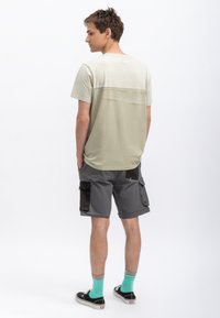 Lichtgroene t-shirt met korte mouwen en een contrasterende horizontale streep; gecombineerd met grijze cargo shorts met donkere accenten en zakken.