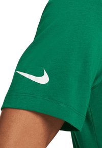 Zelené bavlněné tričko s kulatým výstřihem a krátkými rukávy, s bílým logem Nike na levém rukávu. Hladká textura.
