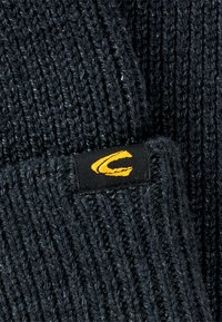 Skręcony ciemnoszary materiał z prążkowaną teksturą, z czarną metką z żółtym logo "C". Brak dodatkowych wzorów lub detali widocznych.