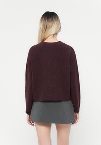 Bordowy sweter o kroju cropped z długimi rękawami, prążkowanym dołem i miękką fakturą, w połączeniu z szaro mini spódnicą. Prosty, minimalistyczny design.