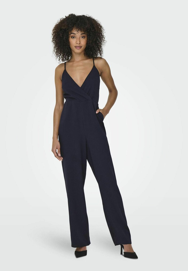 Marinblå jumpsuit med djup V-hals, tunna axelremmar och vida ben. Har en inslagningdesign och sidofickor, tillverkad av ett lätt tyg.