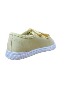 Zapatilla de lona amarilla con suela de goma blanca y agarre texturizado. Presenta un upper cosido y un lazo para facilitar su uso. Nombre de la marca en el lateral.