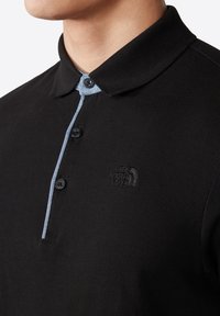 Czarna koszulka polo z teksturowanej tkaniny, z niebieskim akcentem na kołnierzyku i trzema czarnymi guzikami. Haftowane logo na piersi.