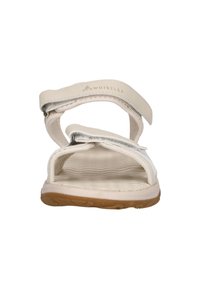 Valkoiset sandaalit, joissa on teksturoitu pohja, säädettävät velcro-hihnat ja joustava kumipohja. Brändäys näkyvissä hihnassa.