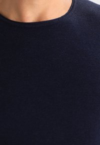 Le t-shirt bleu marine présente un col rond, une texture lisse, et une coupe ajustée, fabriqué à partir d'un tissu doux et extensible.