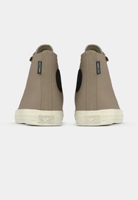 Beige High-Top-Sneakers mit texturierter Oberfläche, schwarzen runden Akzenten und weißen Gummisohlen. Mit Converse All Star-Logo an der Ferse.