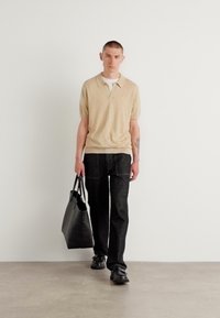 Polo din tricot bej cu mânecă scurtă, asortat cu pantaloni negri lejeri. Geantă de umăr neagră, încălțări închise, design simplu, texturi fine.