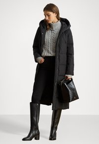 Garšs melns pūkains mētelis ar kapuci, uzvilkts virs pelēka adīta džempera. Melnas šaurās džinsas un augstpapēžu zābaki līdz ceļgaliem. Melnā soma ar krokodila rakstu.