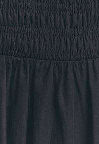 Tela negra con un patrón texturizado y fruncido. El material parece suave con un smocking elástico en la cintura, creando un caída fluida.