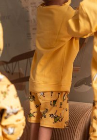 Gelbes Kapuzenset mit Shorts, das verspielte Tierillustrationen zeigt. Die Shorts haben eine Tasche und bestehen aus einem weichen, strukturierten Stoff.
