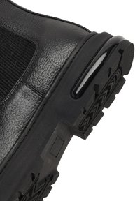 Bota de tobillo de cuero negro con paneles laterales elásticos y una suela de goma texturizada con un patrón en zigzag. Acabado liso con acentos brillantes.