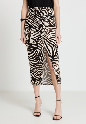 Femme portant une jupe midi à motif zèbre noir et blanc avec une fente à l'avant et un détail boucle, associée à des talons noirs à bride à la cheville.