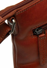 Borsa a tracolla in pelle marrone con una texture liscia, dotata di chiusura con zip, accessori in metallo e un'etichetta con marchio in rilievo.